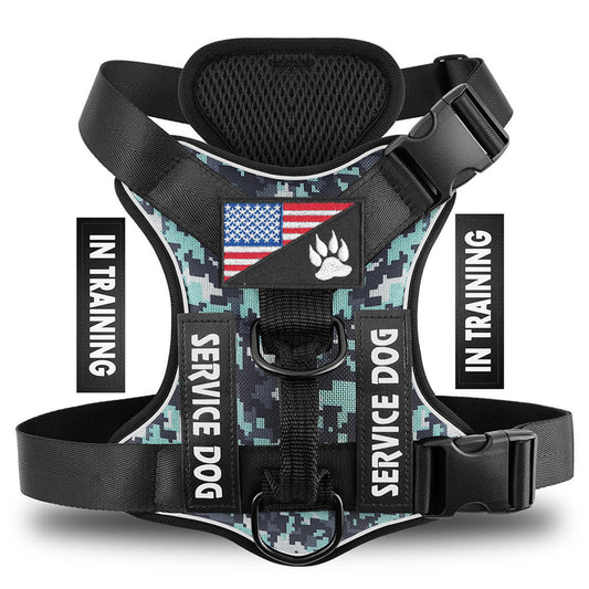 A digital camouflage dog harness with black adjustable straps and plastic buckles, featuring a central patch with an American flag and a paw print, and 'SERVICE DOG' text patches on the sides. The image includes vertical 'IN TRAINING' text overlays on both sides.
